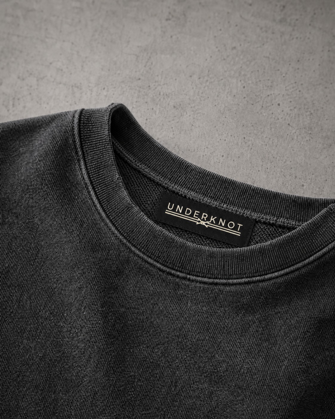 WASHED CHARCOAL 넥 안쪽 중앙의 블랙 직조 UNDERKNOT 메인라벨과 웜 에크루 엠블럼을 보여 주는 디지털 디테일. 사이즈 표기 없음