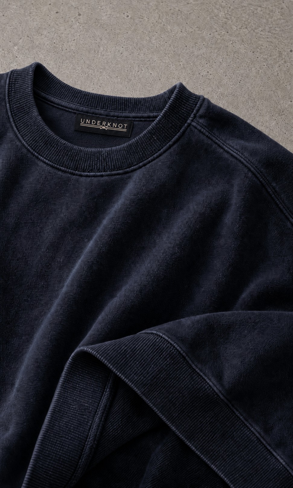 WASHED NAVY 넥 안쪽 중앙의 블랙 직조 UNDERKNOT 메인라벨과 웜 에크루 엠블럼을 보여 주는 디지털 디테일. 사이즈 표기 없음